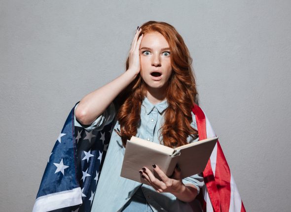 Shocked redhead young lady reading book wearing USA flag