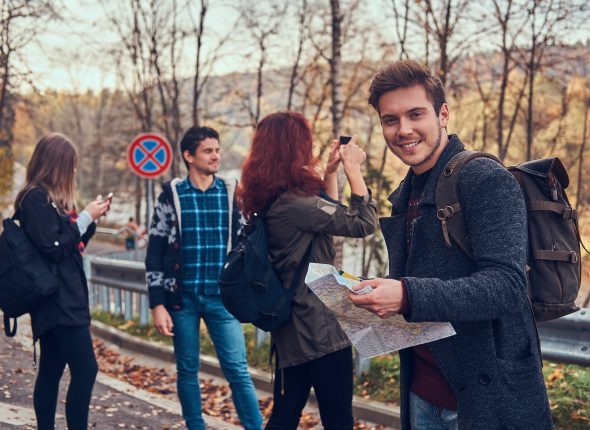 Group of young friends with backpacks sitting next to a road in forest